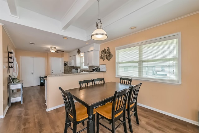 dining room with baseboards, wood finished floors, beam ceiling, and ornamental molding