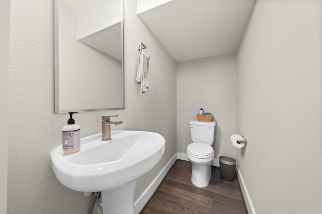 half bathroom with wood finished floors, toilet, baseboards, and a sink