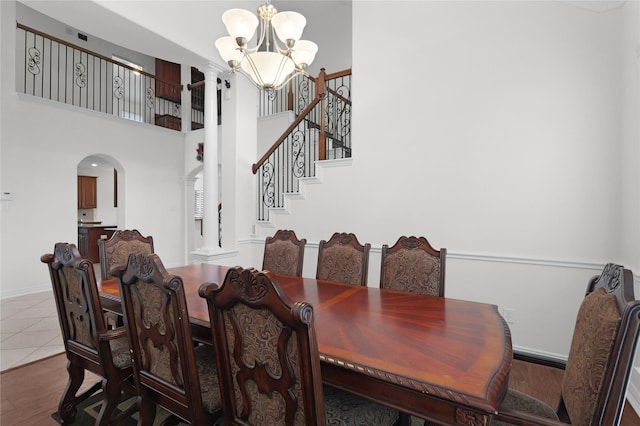dining area with a towering ceiling, wood finished floors, arched walkways, stairs, and a notable chandelier