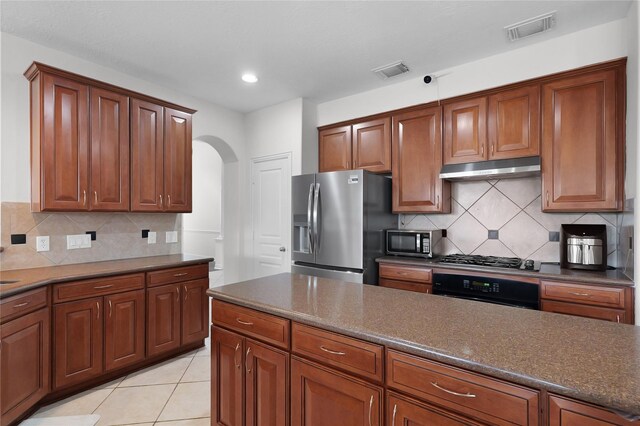 17922 Harbour Bridge Point Dr, Cypress, TX 77429 - kitchen featuring stainless steel appliances, under cabinet range hood, arched walkways, dark countertops, and backsplash