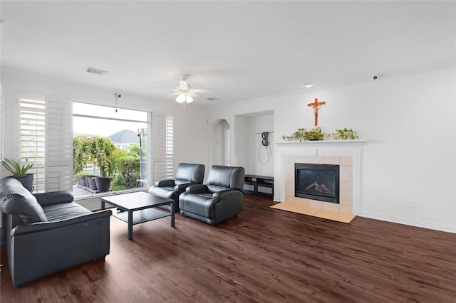 living area with a tile fireplace, ceiling fan, ornamental molding, and wood finished floors