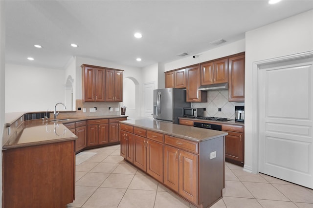 kitchen with stainless steel appliances, a sink, arched walkways, light tile patterned flooring, and tasteful backsplash