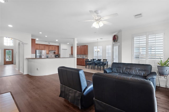 living area featuring a healthy amount of sunlight, wood finished floors, visible vents, and ceiling fan with notable chandelier
