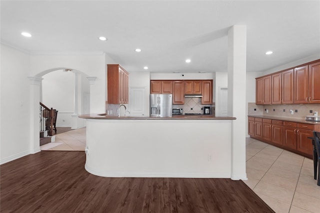 kitchen with tasteful backsplash, a sink, light wood-style floors, arched walkways, and stainless steel fridge with ice dispenser