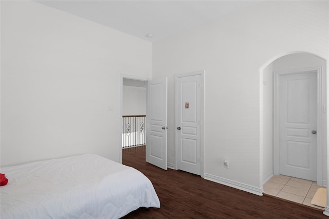 bedroom with arched walkways, wood finished floors, and baseboards