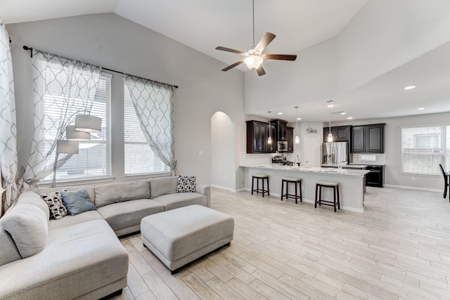 living room featuring high vaulted ceiling, arched walkways, a ceiling fan, and light wood-style flooring