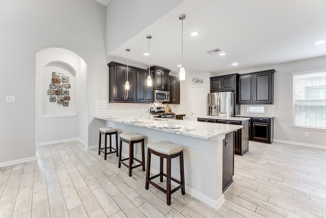 kitchen with light wood finished floors, stainless steel appliances, a peninsula, a kitchen bar, and decorative backsplash