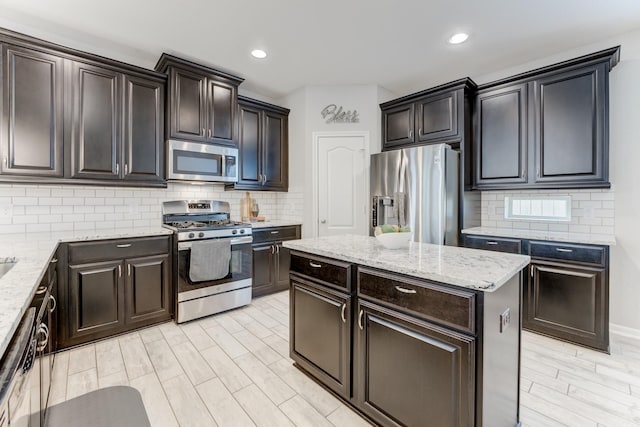 kitchen featuring stainless steel appliances, tasteful backsplash, light wood-type flooring, light stone counters, and a kitchen island