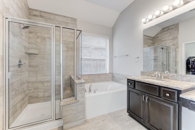 bathroom with a shower stall, vaulted ceiling, vanity, a walk in closet, and a garden tub