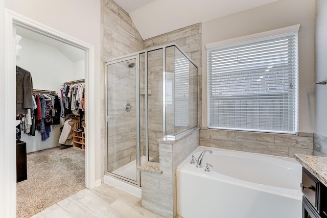 bathroom with a bath, a spacious closet, lofted ceiling, and a stall shower
