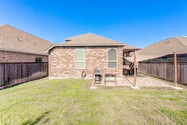 rear view of house with a fenced backyard, roof with shingles, a patio area, a lawn, and brick siding
