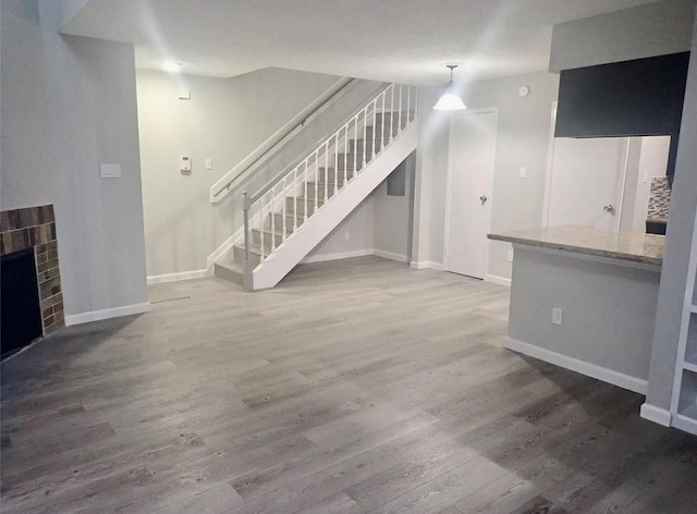 unfurnished living room featuring baseboards, wood finished floors, a fireplace, and stairs