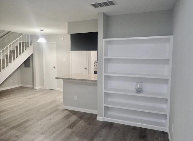 unfurnished living room featuring wood finished floors, visible vents, baseboards, and stairway
