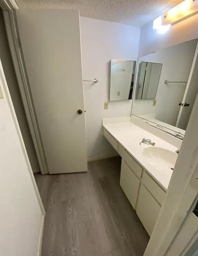 bathroom featuring baseboards, wood finished floors, a textured ceiling, and vanity