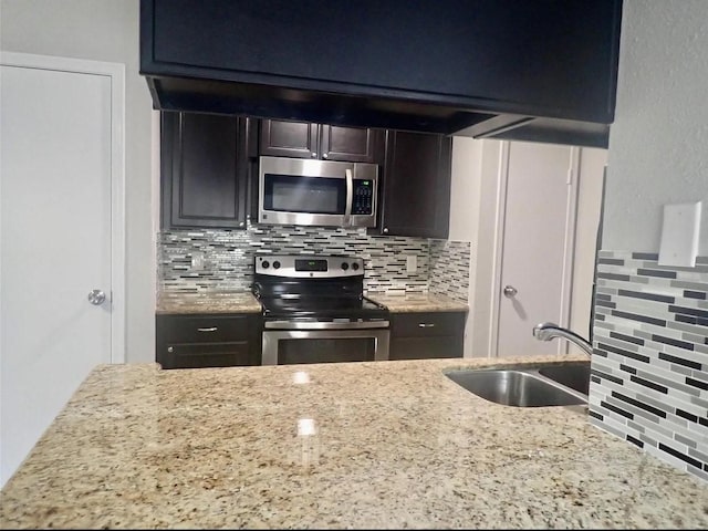 kitchen with light stone countertops, decorative backsplash, a sink, and appliances with stainless steel finishes