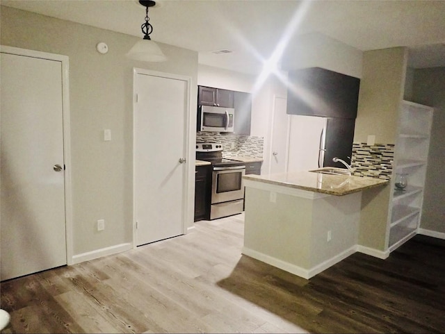 kitchen featuring tasteful backsplash, a sink, hanging light fixtures, light wood finished floors, and appliances with stainless steel finishes