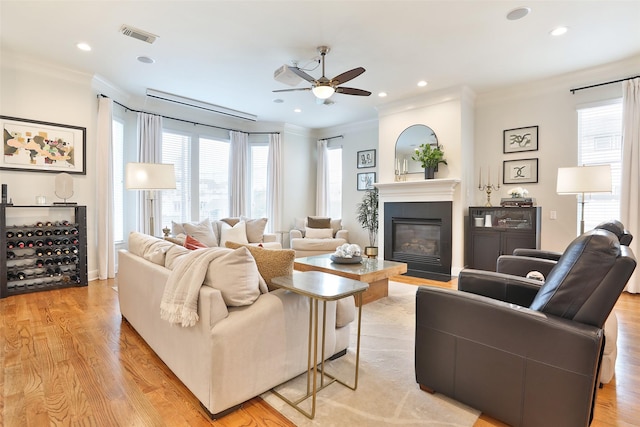 living area featuring ceiling fan, visible vents, ornamental molding, and a glass covered fireplace