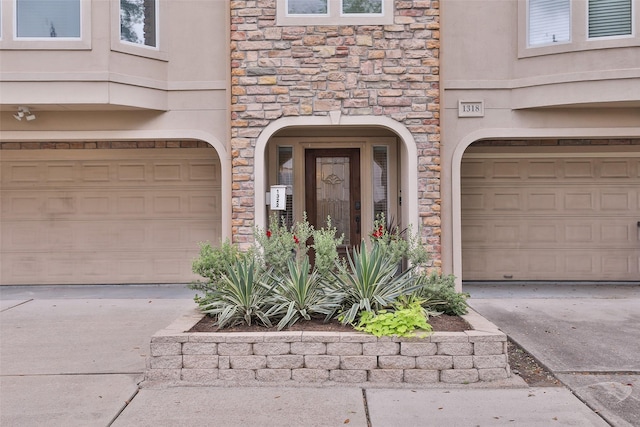 view of exterior entry featuring an attached garage, concrete driveway, and stone siding
