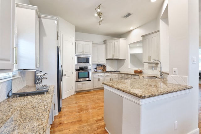 kitchen featuring light wood-type flooring, a sink, decorative backsplash, and stainless steel appliances