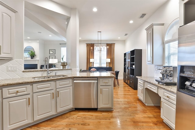 kitchen with appliances with stainless steel finishes, a sink, light wood finished floors, tasteful backsplash, and visible vents