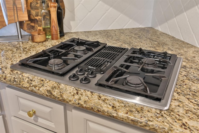 details featuring light stone counters, decorative backsplash, stovetop with downdraft, and white cabinets