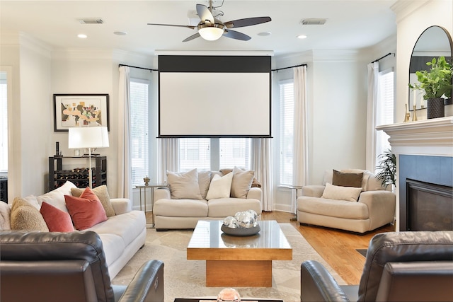 living area with crown molding, ceiling fan, visible vents, and a glass covered fireplace