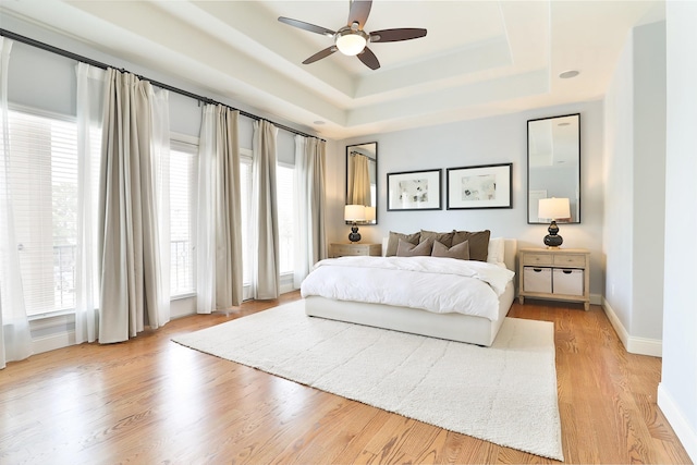 bedroom featuring light wood-type flooring, a ceiling fan, baseboards, and a tray ceiling