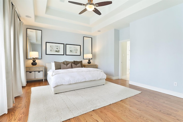 bedroom with baseboards, ceiling fan, wood finished floors, and a tray ceiling