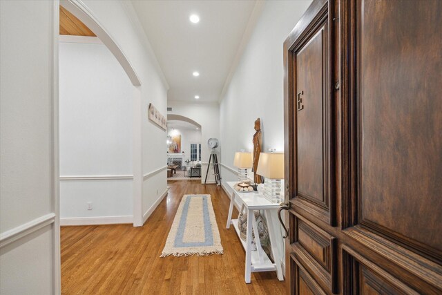 hall featuring light wood-style flooring, baseboards, arched walkways, and recessed lighting