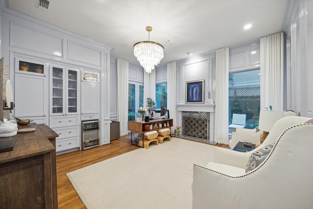 living room with a fireplace with flush hearth, beverage cooler, visible vents, light wood-type flooring, and a notable chandelier