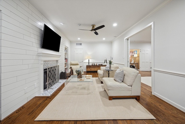 living area featuring wood finished floors, ceiling fan, a fireplace, baseboards, and visible vents