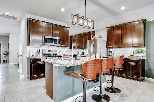 kitchen with a center island with sink, visible vents, decorative backsplash, light stone countertops, and appliances with stainless steel finishes
