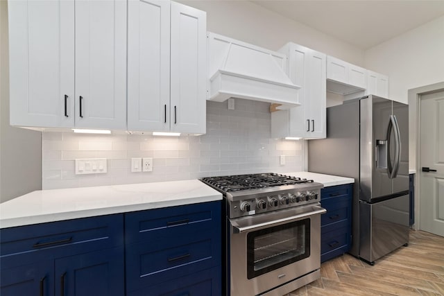 11931 S Red Cedar Cir, The Woodlands, TX 77380 - kitchen featuring stainless steel appliances, blue cabinets, premium range hood, light wood-style floors, and white cabinetry
