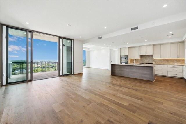 unfurnished living room featuring visible vents, a wall of windows, a sink, and light wood finished floors
