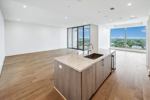 kitchen featuring a wall of windows, a sink, open floor plan, visible vents, and a center island with sink