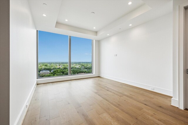 empty room featuring a raised ceiling, baseboards, recessed lighting, and wood finished floors