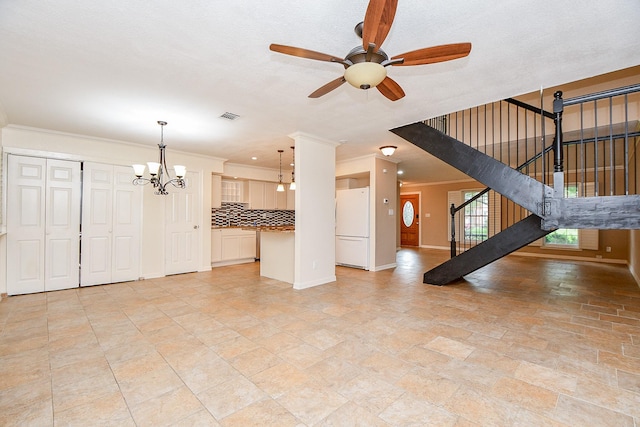 unfurnished living room featuring stairs, ceiling fan with notable chandelier, baseboards, ornamental molding, and visible vents