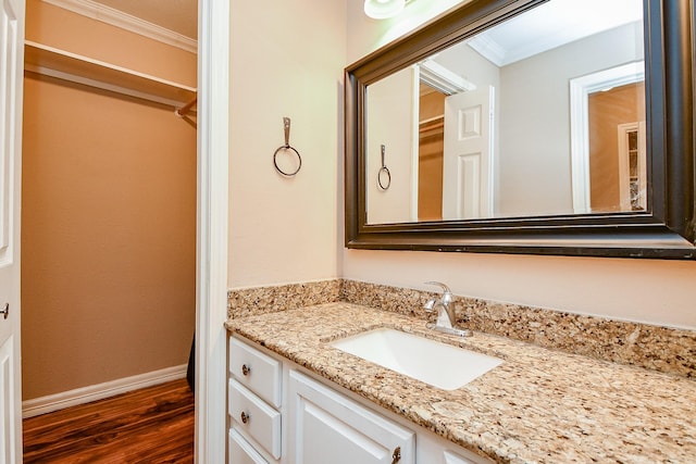 bathroom with wood finished floors, vanity, ornamental molding, and baseboards