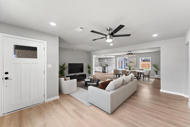 living room featuring light wood-type flooring, baseboards, recessed lighting, and ceiling fan with notable chandelier