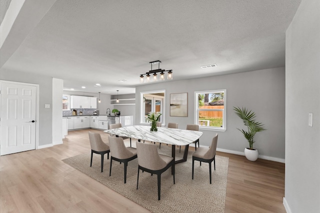dining room with visible vents, baseboards, a textured ceiling, and light wood-type flooring