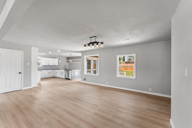 unfurnished living room with visible vents, baseboards, light wood finished floors, and a textured ceiling