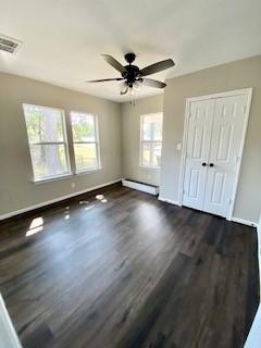 unfurnished bedroom with a baseboard heating unit, baseboards, visible vents, wood finished floors, and a closet