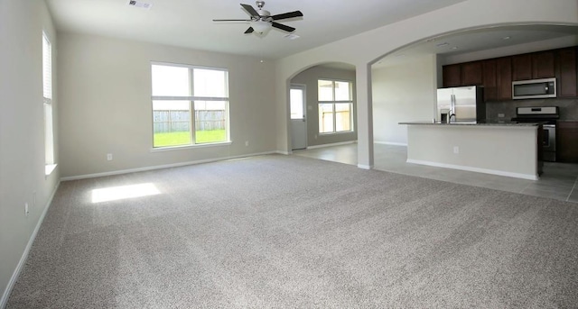 unfurnished living room featuring light colored carpet, ceiling fan, arched walkways, and baseboards