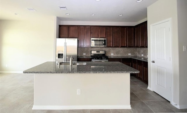 kitchen with tasteful backsplash, dark stone countertops, tile patterned floors, a sink, and stainless steel appliances