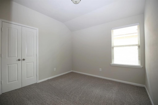 unfurnished bedroom with vaulted ceiling, a closet, carpet flooring, and baseboards
