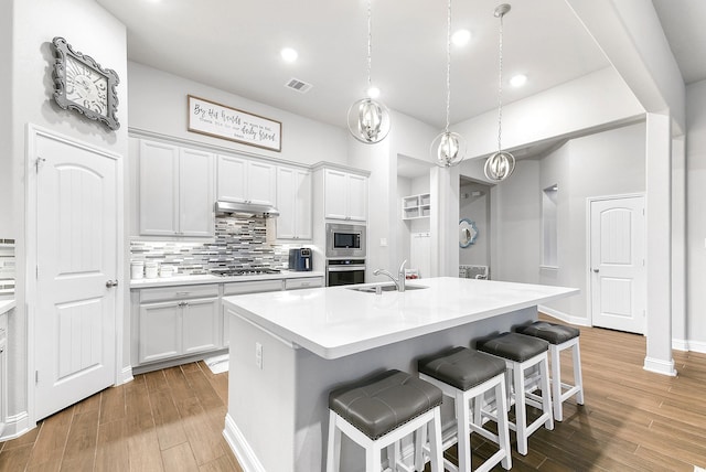 kitchen with light countertops, a sink, light wood-style floors, a breakfast bar, and appliances with stainless steel finishes