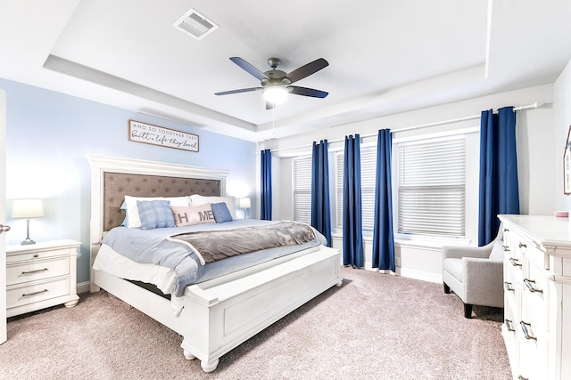 bedroom with visible vents, light carpet, baseboards, and a tray ceiling