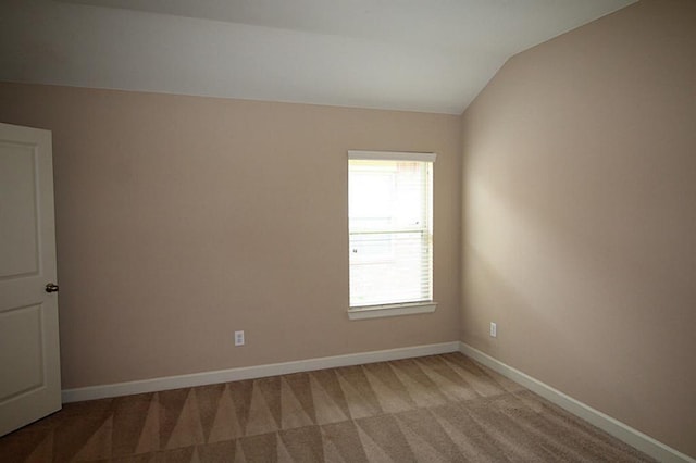 empty room with baseboards, lofted ceiling, and light colored carpet