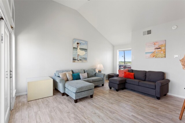 living area featuring high vaulted ceiling, baseboards, visible vents, and light wood-style flooring