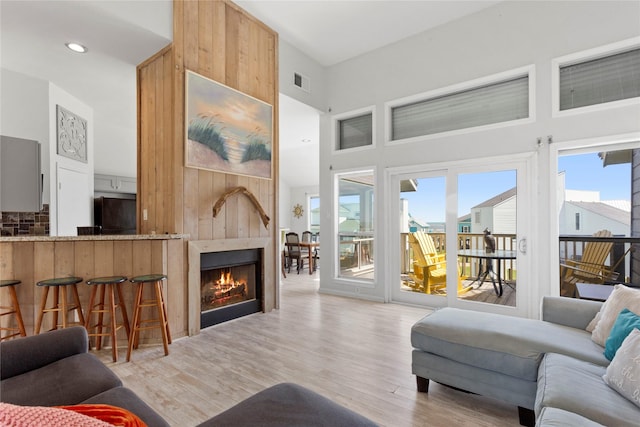 living area featuring wood finished floors, a towering ceiling, a fireplace, visible vents, and recessed lighting